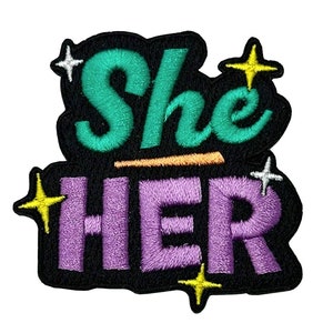 Könnte beinhalten: Ein schwarzer Bügel-Patch mit den Worten "She Her" in lila und türkisfarbener Schrift mit gelben und weißen Sternen.