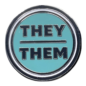 May include: A teal blue enamel pin with a white border and silver metal backing. The pin features the text "THEY/THEM" in black.