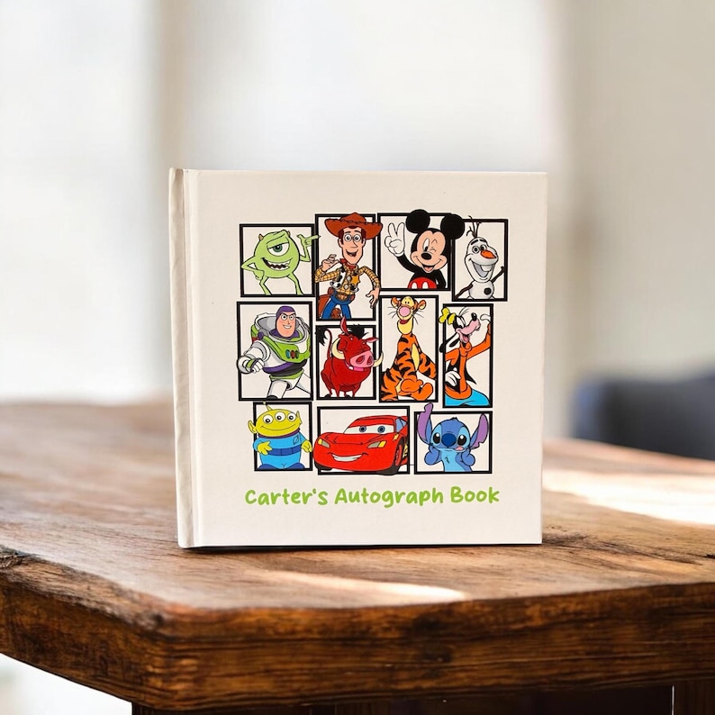 May include: A cream-colored autograph book featuring cartoon characters in black frames. The cover displays characters like Mickey Mouse, Buzz Lightyear, and Lightning McQueen. The text "Carter's Autograph Book" is printed at the bottom in green.