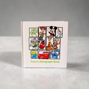 May include: A square, off-white autograph book featuring a collage of Disney cartoon characters in black frames. The book's cover includes characters like Mickey Mouse, Woody, and Lightning McQueen. The text "Enzo's Autograph Book" is printed at the bottom.