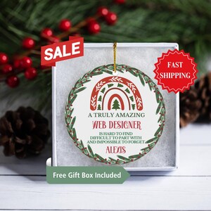 May include: A round, white Christmas ornament with a green wreath border. The ornament features a red and green rainbow with a pine tree in the center. The text reads "A truly amazing web designer is hard to find, difficult to part with and impossible to forget, Alexis".