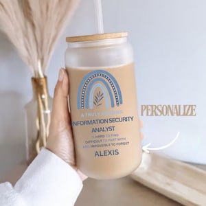 May include: A brown and white reusable tumbler with a bamboo lid and a straw. The tumbler has a blue and white rainbow design with a leaf and the text "A Truly Amazing Information Security Analyst is hard to find, difficult to part with and impossible to forget, Alexis".