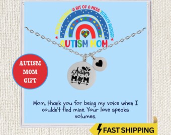 May include: A silver necklace with two charms. One charm is a round pendant with the words "Autism Mom" and a symbol. The other charm is a small circle with a black heart. The necklace is on a blue card with text and a rainbow design.