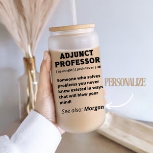 May include: A glass tumbler with a bamboo lid and straw, featuring the text "ADJUNCT PROFESSOR" with a definition. The definition reads, "Someone who solves problems you never knew existed in ways that will blow your mind!" The word "PERSONALIZE" is also visible.