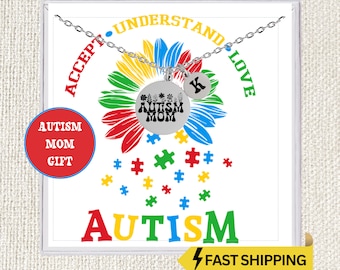 May include: A silver necklace with two pendants. One pendant is round with the words "AUTISM MOM" and floral designs. The other pendant is a small circle with the letter "K". The background features a sunflower design and the word "AUTISM".