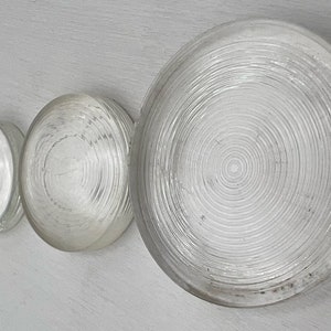 May include: Four clear glass lenses with a concentric circle pattern. The lenses are arranged in a row from smallest to largest.