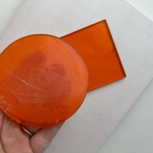 May include: An orange, translucent, circular object and a rectangular object. The circular object has text on it. The objects are on a white surface. The objects are a vibrant orange color.