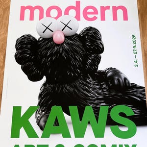 May include: Poster with a black KAWS character, white eyes with cross marks, and a pink nose. The poster displays the text "ALBERTINA modern" in pink and "KAWS ART & COMIX" in green. The date "3.4. - 27.9.2026" is also visible.