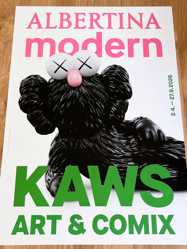 May include: Poster with a black KAWS character, white eyes with cross marks, and a pink nose. The poster displays the text "ALBERTINA modern" in pink and "KAWS ART & COMIX" in green. The date "3.4. - 27.9.2026" is also visible.