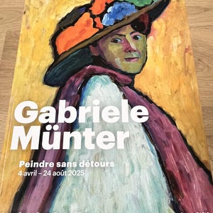 Könnte beinhalten: Plakat für die Gabriele Münter Ausstellung im Musée d'Art Moderne de Paris. Das Kunstwerk zeigt ein Porträt einer Person mit buntem Hut und Schal. Das Plakat enthält die Ausstellungsdaten und Museumsinformationen.