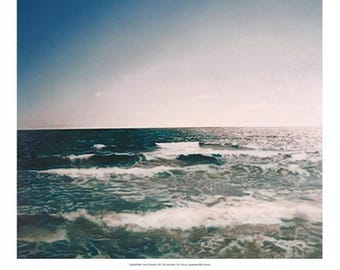 以下が含まれることがあります： 青い空と白い波立つ海の写真。写真は低い角度から撮影されており、水平線に向かって撮影されています。水は濃い青色で、空は明るい青色です。白い波は小さく、水面に散らばっています。写真は晴れた日に撮影され、太陽が明るく輝いています。写真は、美しく穏やかな海の描写です。