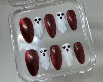 May include: A set of ten press-on nails in a clear plastic case. The nails alternate between a deep red color and white nails with ghost designs. The ghost nails have black eyes and a small mouth.