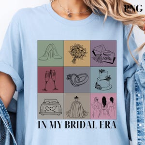 以下が含まれることがあります： 薄い青色のTシャツに、9つの正方形のグリッドで構成されたグラフィックデザインが施されています。各正方形には、靴、シャンパンフルート、花束、ウェディングケーキ、指輪、車、ウェディングドレス、2人のブライズメイドなど、結婚式に関連するさまざまなイラストが描かれています。グリッドの下には「In My Bridal Era」というテキストが印刷されています。