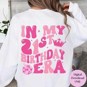 May include: White sweatshirt with pink text that reads "In My 21st Birthday Era" with a pink disco ball and crown graphic.