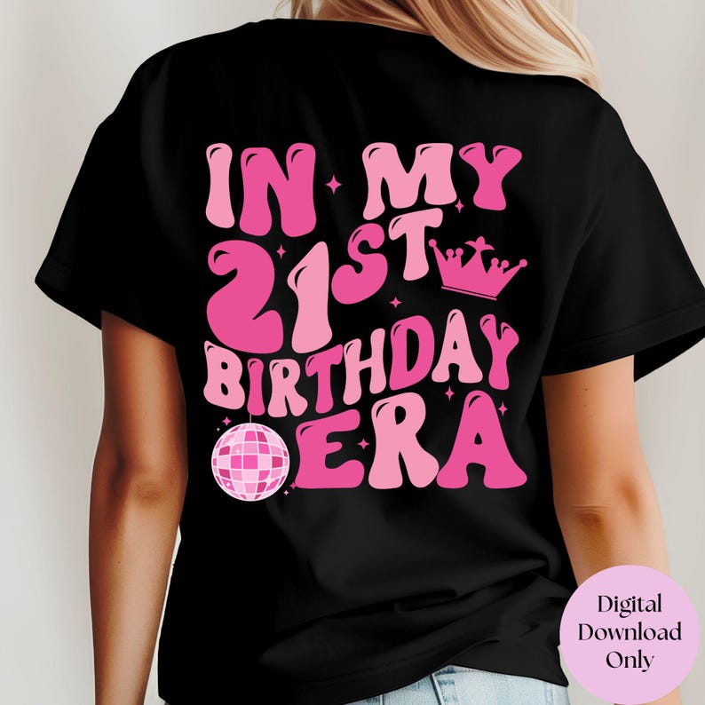 May include: Black t-shirt with pink text that says "In My 21st Birthday Era" with a pink disco ball and crown graphic.