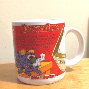 May include: A white ceramic mug featuring a red background with the text "Downtime" and a definition of the term. The design includes a cartoon blue creature and a computer illustration with the text "Bits & Bytes" at the bottom.