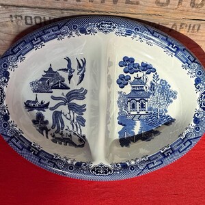 May include: Oval serving dish with a blue and white Willow pattern. The dish is divided into two sections and features a detailed landscape design with pagodas, trees, and bridges. The rim has a decorative border.