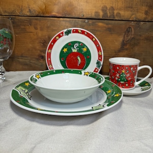 May include: A set of Christmas themed dinnerware featuring a green and red design with a white background. The set includes a bowl, a plate, a saucer, and a mug.