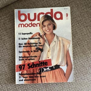 Può includere: Una rivista vintage Burda Moden del marzo 1985 con l'immagine di copertina di una persona che indossa una camicetta a righe di colore chiaro e una gonna color pesca con una cintura nera. La copertina include testo come 12 Superpullis, 11 Seiten Kombimode e 97 Schnitte.