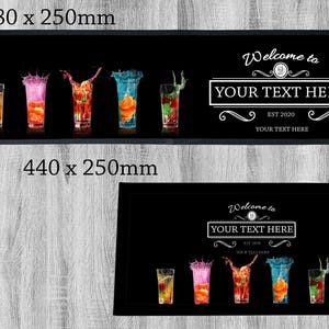May include: Black bar mat with a welcome to your text here design. The bar mat features a black background with white text and a decorative design. The bar mat also features a row of five colourful cocktails with splashes of liquid.