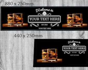 May include: Black bar mat with the text "Welcome to YOUR TEXT HERE EST 2020 YOUR TEXT HERE" and two glasses of amber liquid. The bar mat is available in two sizes: 880 x 250 mm and 440 x 250 mm.