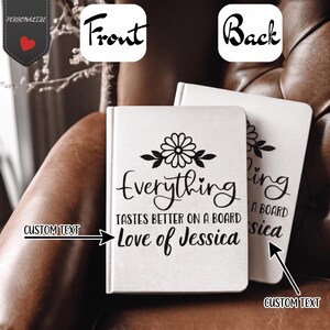 May include: Two white notebooks with black text and floral designs. The front notebook reads "Everything tastes better on a board Love of Jessica." The back notebook has the text "ling a board sica." The notebooks are on a brown surface.