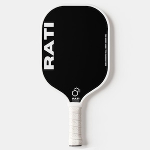 May include: A white and black pickleball paddle with the word "RATI" printed in white on the black face. The paddle has a white grip with a textured pattern.