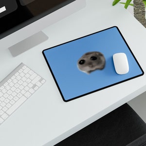 May include: A blue mouse pad with a white mouse and a blurry image of a hamster on it. The mouse pad is on a white desk with a keyboard and a computer monitor with a digital clock that reads "2:16 PM".