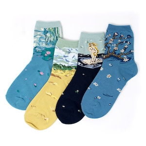 May include: Four pairs of crew socks with art-inspired designs. Each sock features a different painting: water lilies, a beach scene, Botticelli's Venus, and a flowering tree. The socks are in shades of blue, yellow, and navy.