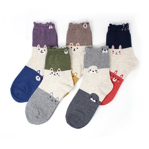 May include: A collection of six pairs of novelty socks. Each pair features a two-tone design with a solid color on the toe and heel, and a neutral color on the foot and leg. The socks are decorated with embroidered animal faces, including cats, bears, and a rabbit.