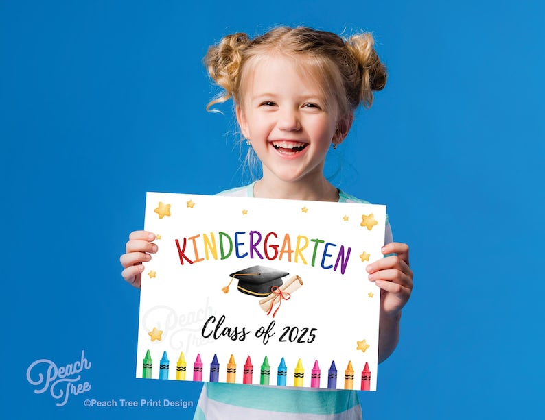 May include: A smiling child holds a white sign with the word "Kindergarten" in rainbow colors. The sign features a graduation cap, diploma, and the text "Class of 2025", with colorful crayons at the bottom and star accents.