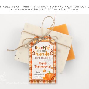 Op de afbeelding: Een Thanksgiving-cadeaulabel met de tekst "dankbaar voor de handen die me leren". Het label is oranje en wit geruit, vastgebonden met touw aan twee stukken zeep. Een pompoen en bladeren staan onderaan.
