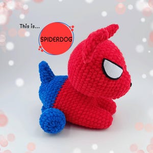 Può includere: Un peluche Spiderdog fatto a mano, rosso e blu. Il peluche è lavorato all'uncinetto con una testa e un corpo rossi, quarti posteriori blu e dettagli degli occhi bianchi. Il testo "This is... SPIDERDOG" è sullo sfondo.