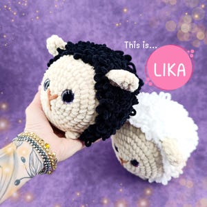 Può includere: Due peluche di pecora all'uncinetto, uno con la pelliccia nera e uno con la pelliccia bianca. Entrambi hanno il corpo beige e gli occhi neri. Il testo "This is... LIKA" è in un cerchio rosa.