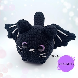 Può includere: Un pipistrello nero all'uncinetto con dettagli bianchi sulle ali e sul viso. Il pipistrello ha grandi occhi viola glitterati e una bocca cucita. Il testo "This is... SPOOKITTY" è in un cerchio viola.