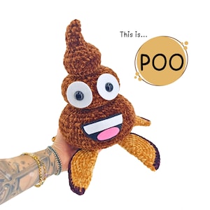 Puede incluir: Un juguete de peluche marrón tejido en forma de emoji de caca sonriente. El juguete tiene ojos blancos grandes con pupilas negras, una boca rosa y brazos y pies pequeños de color canela. El texto "This is... POO" está en una burbuja.