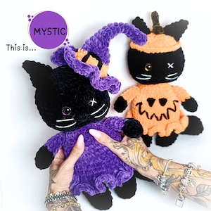Può includere: Due giocattoli di Halloween a forma di gatto nero all'uncinetto. Un gatto indossa un cappello da strega viola e l'altro un costume da zucca arancione. "This is... MYSTIC" è scritto in viola su sfondo bianco.