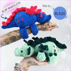 Peut inclure: Deux jouets en crochet en forme de dinosaure. Le dinosaure bleu a des piques rouges et dit "SLAP BRACELET!!" Le dinosaure vert a des piques vert foncé et dit "This is... BLAZE".
