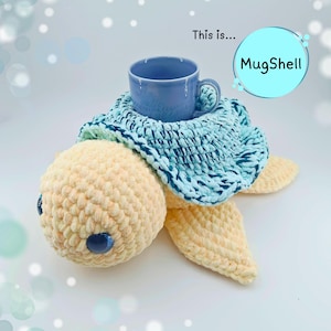 May include: A handmade crochet turtle with a blue mug nestled in its shell. The turtle is primarily cream-colored with blue accents, including the eyes and the shell's trim. The text "MugShell" is in a blue circle.