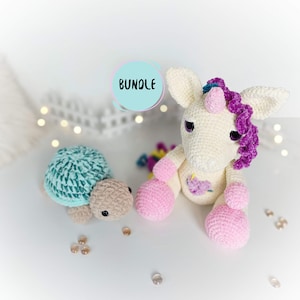 Può includere: Un giocattolo di unicorno all'uncinetto con una criniera rosa e zoccoli rosa, seduto accanto a un giocattolo di tartaruga all'uncinetto con un guscio turchese. I giocattoli sono su una superficie bianca con un cerchio blu chiaro con la parola "BUNDLE" in testo bianco.