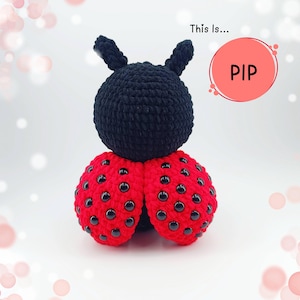 Può includere: Un giocattolo a forma di coccinella fatto a mano all'uncinetto. La coccinella ha una testa e antenne nere, con ali rosse punteggiate di punti neri. Il testo "This Is... PIP" è in un cerchio rosa.