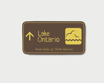 May include: A rectangular brown sign with a yellow border featuring an upward-pointing arrow, the text Lake Ontario, and a yellow square icon depicting stylized waves and birds. Below, the text reads Great Lakes of North America.