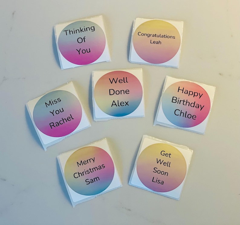 Puede incluir: Ocho pegatinas cuadradas de colores con esquinas redondeadas y fondo blanco. Cada pegatina tiene un mensaje y un nombre diferentes, como "Thinking of You", "Congratulations Leah", "Miss You Rachel", "Well Done Alex", "Happy Birthday Chloe", "Merry Christmas Sam", "Get Well Soon Lisa".