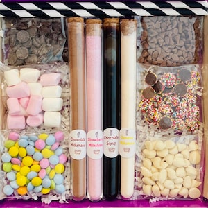 Puede incluir: Una caja de regalo llena de ingredientes para hacer batidos. La caja incluye mezclas de batidos de chocolate, fresa y plátano, jarabe de chocolate, malvaviscos, chispas de chocolate, chispas de chocolate blanco y chispas.