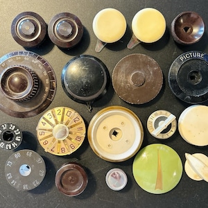 May include: A collection of vintage radio knobs in various shapes, sizes, and colors. The knobs are made of materials like bakelite and plastic, with some featuring numbers and markings. Includes knobs with the word "PICTURE".
