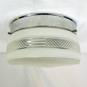 May include: A flush mount ceiling light fixture featuring a polished chrome metal base and a cylindrical glass shade. The glass shade has a frosted finish with a clear, textured band around the center that displays a repeating diamond pattern.