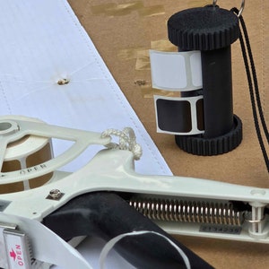 May include: A white and black label maker with a roll of labels and a separate label dispenser. The label dispenser has a black cord and a white label with the word "OPEN" printed on it. The label maker has a spring and a serial number "2134235".