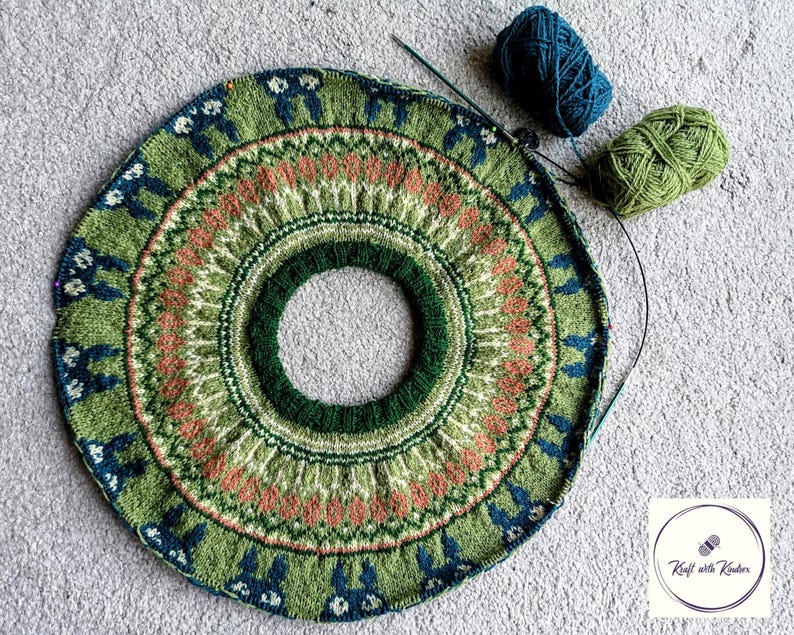 May include: Circular knitted project in progress, featuring a detailed pattern in shades of green, coral, and blue. The design includes repeating motifs and a central opening. Two balls of yarn, one teal and one green, are next to the project.