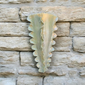 May include: A ceramic wall vase with a scalloped edge and a light green glaze. The vase is mounted on a stone wall.