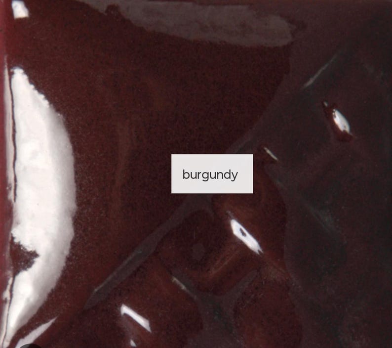 Op de afbeelding: Een glad, glanzend oppervlak met een diepe bordeauxrode kleur. Een wit rechthoekig label is in het midden van de afbeelding geplaatst, met het woord burgundy in zwarte, schreefloze kleine letters. De afwerking is reflecterend.